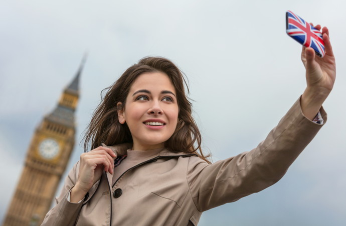 Girl or young woman tourist on vacation taking a selfie photograph by Big Ben with Union Jack cell phone, London, England, Great Britain